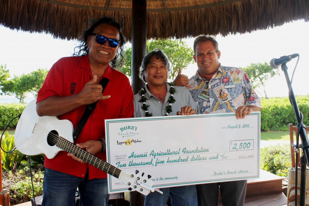 Duke's Beach House presented the Hawai'i Agricultural Foundation with a $2,500 check at the Henry Kapono performance. Pictured left to right: Henry Kapono, Warren Watanabe, Hawai'i Agricultural Foundation; John Brans, Duke’s Beach House Manager. Photo Courtesy. 