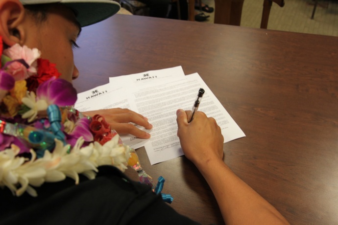 Baldwin's Keelan Ewaliko puts the pen to the paper Wednesday, signing his letter of intent to play football for Hawaii. Photo by Ben Juan.