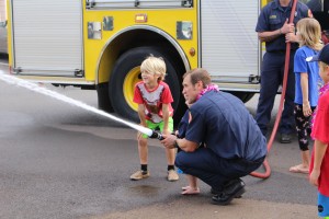 Trucker Dukes shooting water with his dad, firefighter Joshua Dukes and his brother outside of the Kahului Fire Station. Photo by Wendy Osher.