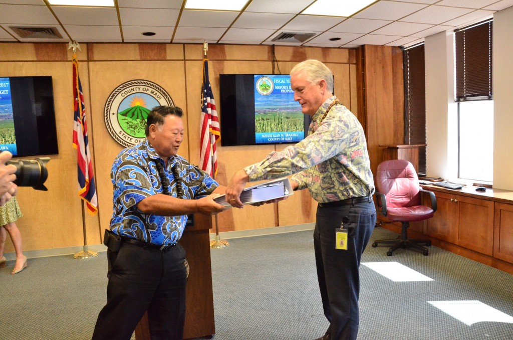 Maui Mayor Alan Arakawa (left) hands off his version of the Fiscal Year 2017 budget to Maui Council Chair Mike White (left). Photo credit: Maui Office of Council Services.